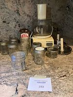 Photo of Cuisinart food processor with bowl, feed tube, pushers, slicing discs and assorted mason jars with lids.
