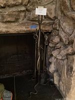 Fireplace tool set against stone fireplace, showing snake-like twisted metal stand and tools.