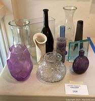 Full view of the assorted flower vases showing various colors, shapes and materials including clear, purple, black, and white vases in glass and ceramic.