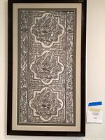 Front view of framed monochrome Indian tapestry on white wall showing full piece with dark brown frame and linen mat