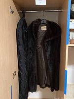 Long dark brown/black fur coat hanging inside closet, lining exposed