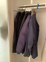 Side view of four men's jackets hanging, showing variety of materials and colors.