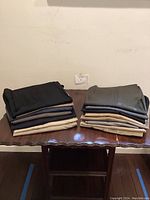Two stacks of folded men's slacks in assorted colors on a wooden table.