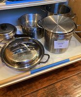 Overview of different stainless steel pots, pans, and strainers showing lids and handles.
