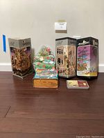 Lot of puzzles arranged against a wall showing 3 large 1000-piece puzzle boxes, a wooden Christmas tree puzzle, a 500-piece Dowdle San Diego puzzle box and additional small tins or boxes.