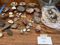 Photo showing various rocks including geodes, polished stones, shale, slate, and two metal buckets on a wooden surface.