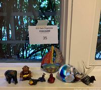 Photo shows a collection of small animal and decorative figurines arranged on a windowsill in natural light including elephant, monkey, birds, glass whale, boat.