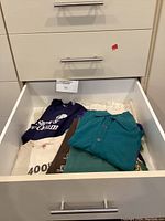 Open drawer showing folded men's shirts including t-shirts and collared shirts in various colors and styles