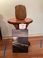 Photo of the round wood table with the handmade vase displayed on top and the ocean canvas picture placed against the table front.