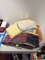 Pile of folded textiles including yellow napkins on top, white beaded doily with green border, and multi-colored embroidered textile underneath.
