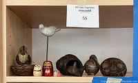 Shelf with assorted carved and ceramic figurines including ceramic pelican dish, stone face sculpture, Russian dolls, and wood animals