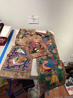 Four painted cloth art pieces laid out on a table showing colorful bird and floral designs from Uruguay