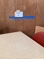 Corner view of cream laminate surface of the card table and part of one burnt orange cushioned chair with wooden backrest.