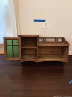 Full front view of the wooden wall cabinet with one green glass door open showing two shelves inside and one open shelf on the right side