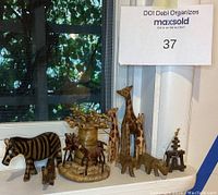 Set of wooden animal figurines including zebras, giraffes, rhinos, and trees displayed on a windowsill, visible natural wood tones and hand-painted details.