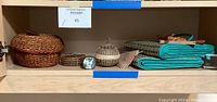 Shelf with baskets, woven cage container, coasters, folded beach mats in teal and natural tones.