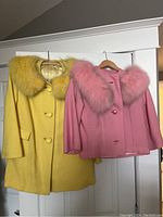 Two faux fur coats hanging on door, yellow and pink, showing overall appearance and color.