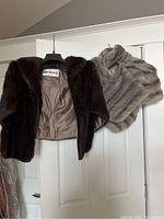 Two fur shawls hanging on door, brown labeled Woodwards and grey unnamed brand