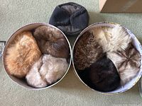 Top view of 7 vintage fur hats inside two different round hat boxes and one additional dark fabric hat placed outside the boxes.
