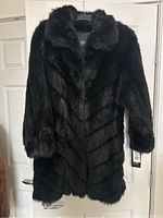 Front view of black faux fur jacket on door with visible chevron pattern and broad collar.