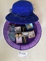 Box showing blue felt hat with feather, multiple boxes of costume jewelry including earrings and bracelets