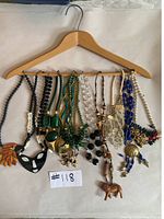 All 11 necklaces hanging on wooden hanger showing full variety of costume jewelry with different pendants and bead styles.