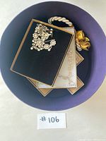 View of the boxed rhinestone costume jewelry with necklace and earrings inside a purple container with ropes and a yellow flower.