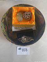 Round floral patterned hat box holding various pieces of costume jewelry inside.