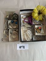Two plastic containers filled with assorted costume jewelry including earrings, bracelets, and necklaces of various colors and styles.