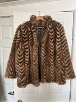 Front view of brown faux fur coat with black chevron pattern hanging on wooden hanger against white door.