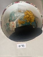 Open floral-patterned hat box showing the black feather hat and turquoise-colored jewelry inside.