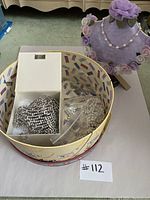 Lot overview showing decorative round hat box holding jewelry and purple floral necklace display.
