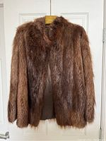Front view of the brown real fur coat hanging on a wooden hanger against a white door, showing the thickness and softness of the fur.