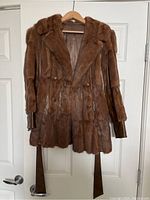 Front view of vintage brown fur and leather jacket, showing fur texture, buttons, and hanging leather belt.