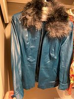 Front view of blue leather jacket with dark fur collar held at shoulder, highlighting material and style.