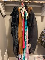 Side view of assorted women's clothing items hanging in closet including black sequin dress and brown suede fringe vest