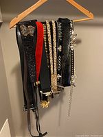 Belts hanging on a wooden hanger showing various styles including black mesh, red velvet, gold-tone and rhinestone details.