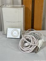 Apple iPod Shuffle 1GB silver model beside the clear plastic original case showing Apple branding on the inside.