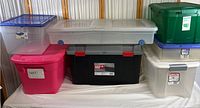 Overall photo showing various plastic storage containers stacked and side by side, different sizes and colors including black and gray container with red handles, pink, clear Sterilite with blue lid, green, and white containers.