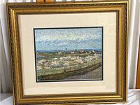 Full view of the ornate gold frame and print of a rural community scene showing houses, blossoming trees, fences, fields, and distant hills.