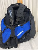 Front view of blue and black Isla Oceanic buoyancy compensator device showing shoulder straps embroidered with ISLA and OCEANIC logo on fabric section.