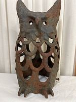 Front view of hollow metal owl decoration with eye cutouts and scale-patterned body.
