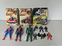 Full view of the toy lot including 13 assorted Batman and Spider-Man toys comprising vehicles and action figures, some in original packaging and some loose on a white surface.