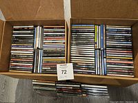 Two cardboard boxes filled with over 100 assorted used CDs stacked vertically, showing cases and some album titles.