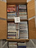 Open cardboard boxes filled with used country music CDs, stacked neatly and visible titles including '70s Country' and multiple artists.