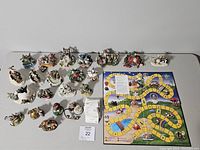Top-down photo showing 20+ Charming Tails animal figurines arranged in rows next to a colorful board game.