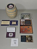 Lot overview showing James Salt Water Taffy barrel coin bank and six coin sets in protective cases arranged on a surface with a lot tag.