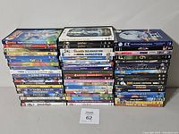 Photo showing a large assorted collection of used DVDs stacked in three columns. Titles visible include various Disney, Dreamworks, and other animated and family films.