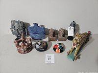 Photo of assorted folk art decor items including stone mask, blue vase, carved sculpture, owls, decorative items and vintage wooden toy.