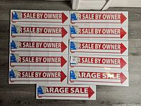 Nine "For Sale By Owner" signs and two "Garage Sale" signs sealed in plastic with metal stakes attached.